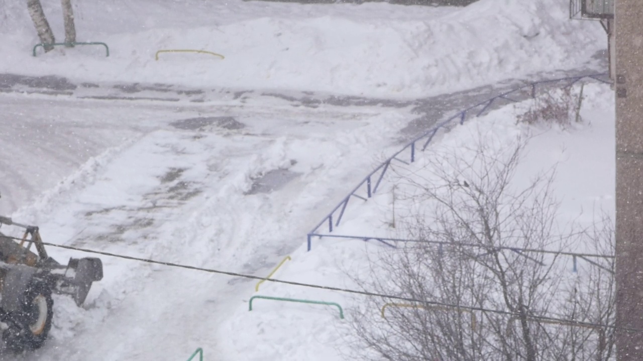 一辆带着铲斗的拖拉机正在清除住宅区院子里堆积的积雪。冬天下雪的一天，一辆推土机正在清理道路。公用事业和交通工具。暴雨雪视频素材