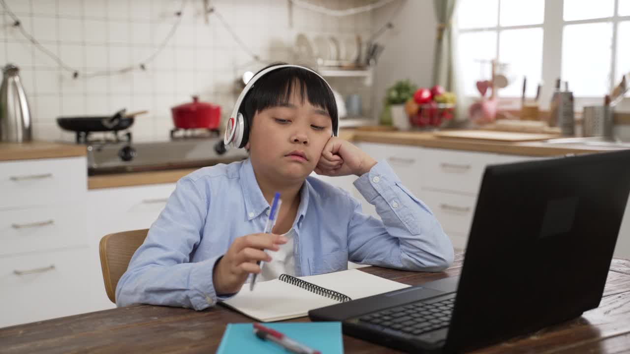 十几岁的韩国男孩对在线学习感到厌烦，使用互联网，戴上耳机，在家转笔。教育与知识现代科技理念视频素材