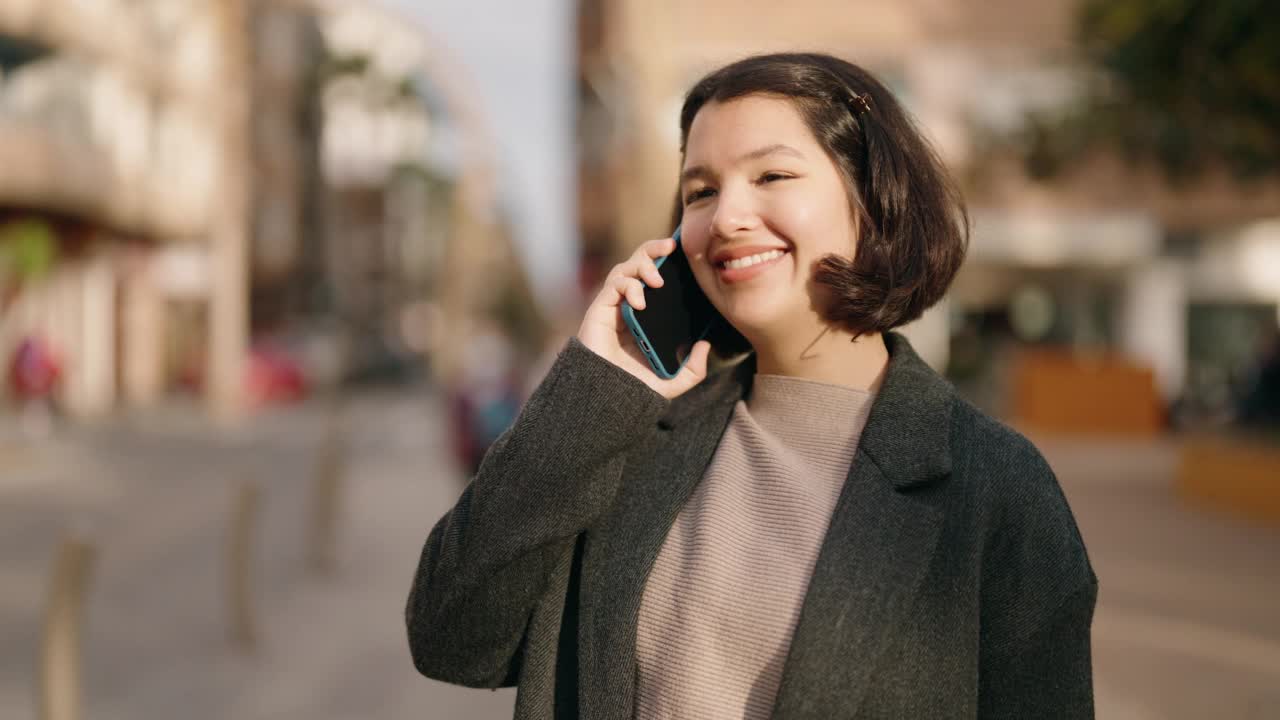 年轻的西班牙女孩微笑着自信地在街上用智能手机聊天视频素材