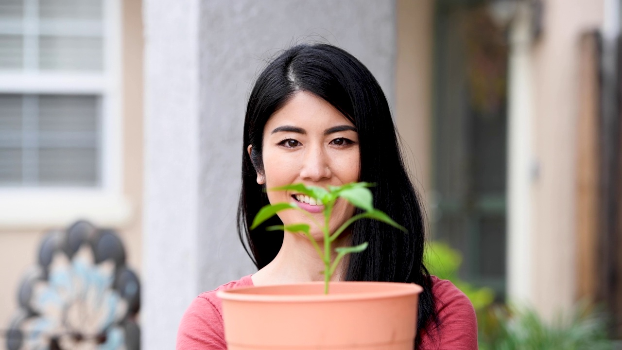 一个亚洲女人微笑着摆姿势看着镜头，手里拿着一盆植物视频素材