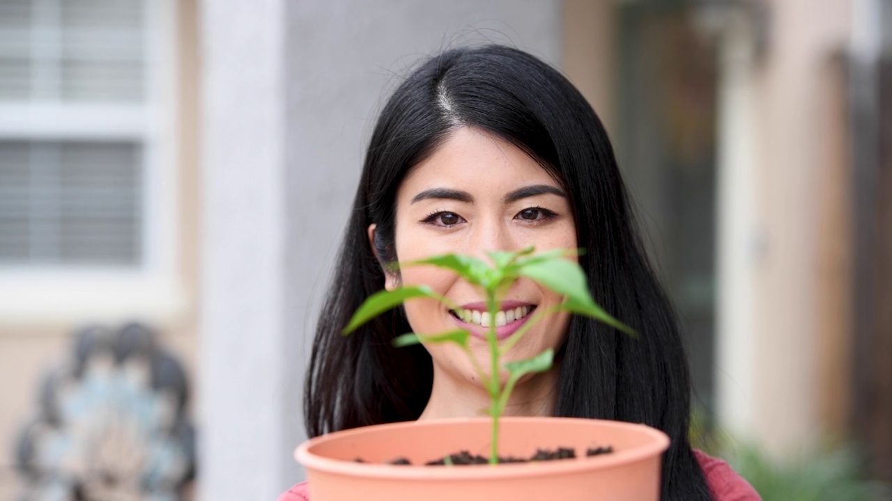 一个亚洲女人微笑着摆姿势看着镜头，手里拿着一盆植物视频素材