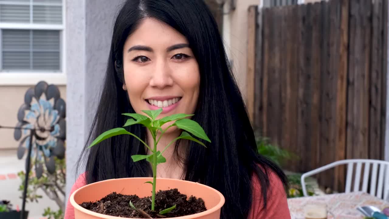 一个亚洲女人微笑着摆姿势看着镜头，手里拿着一盆植物视频素材