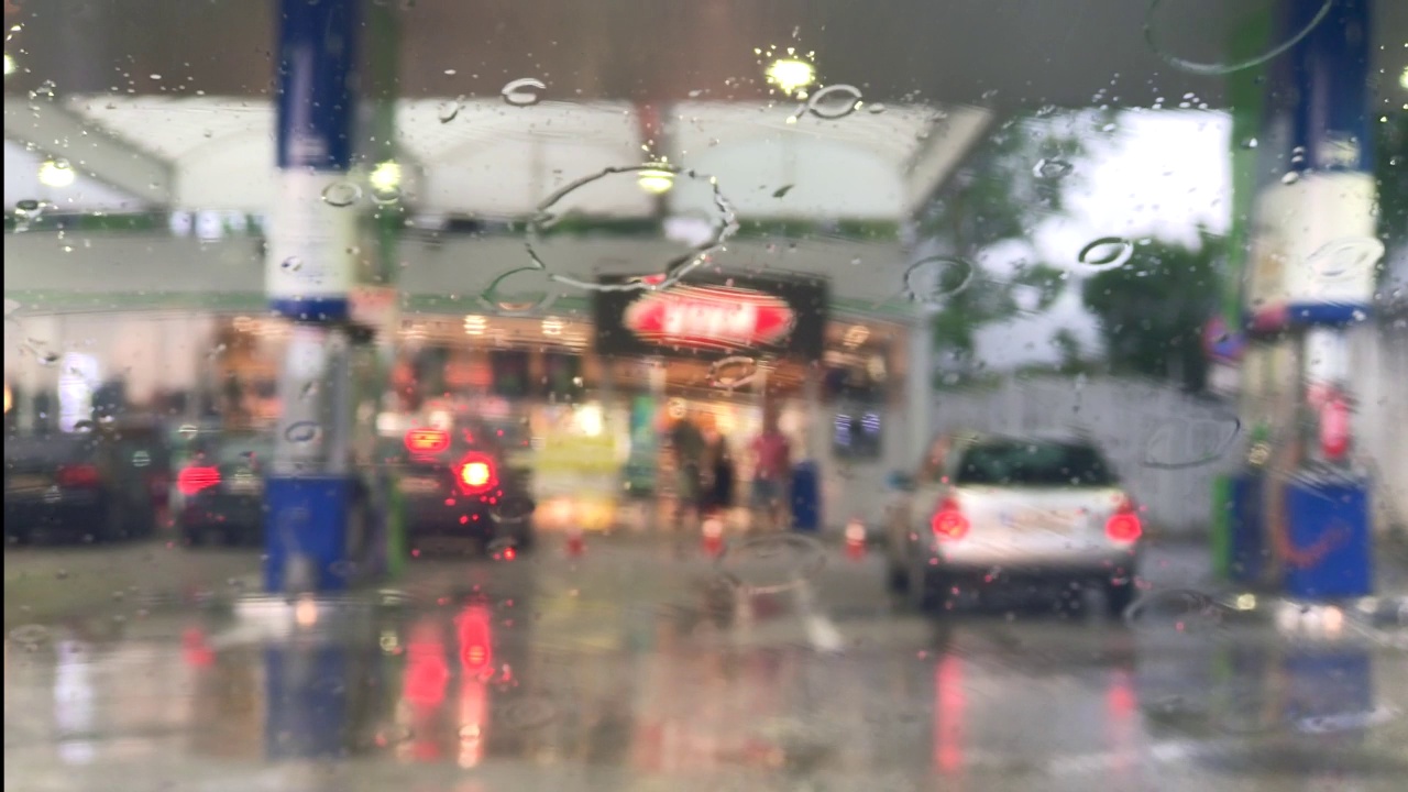 模糊的加油站背景，雨滴落在车窗上。雨刷的动作。视频素材