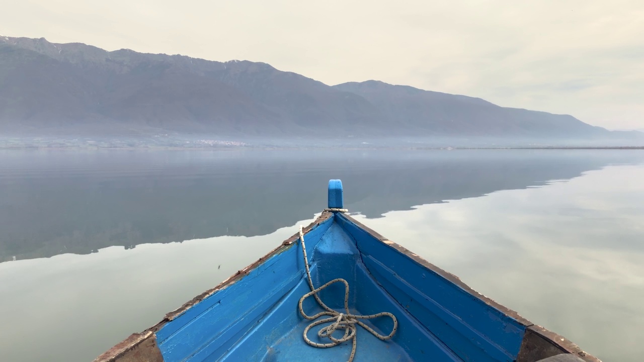 蓝色的小船漂浮在平静的湖面上，远处有一座山视频下载