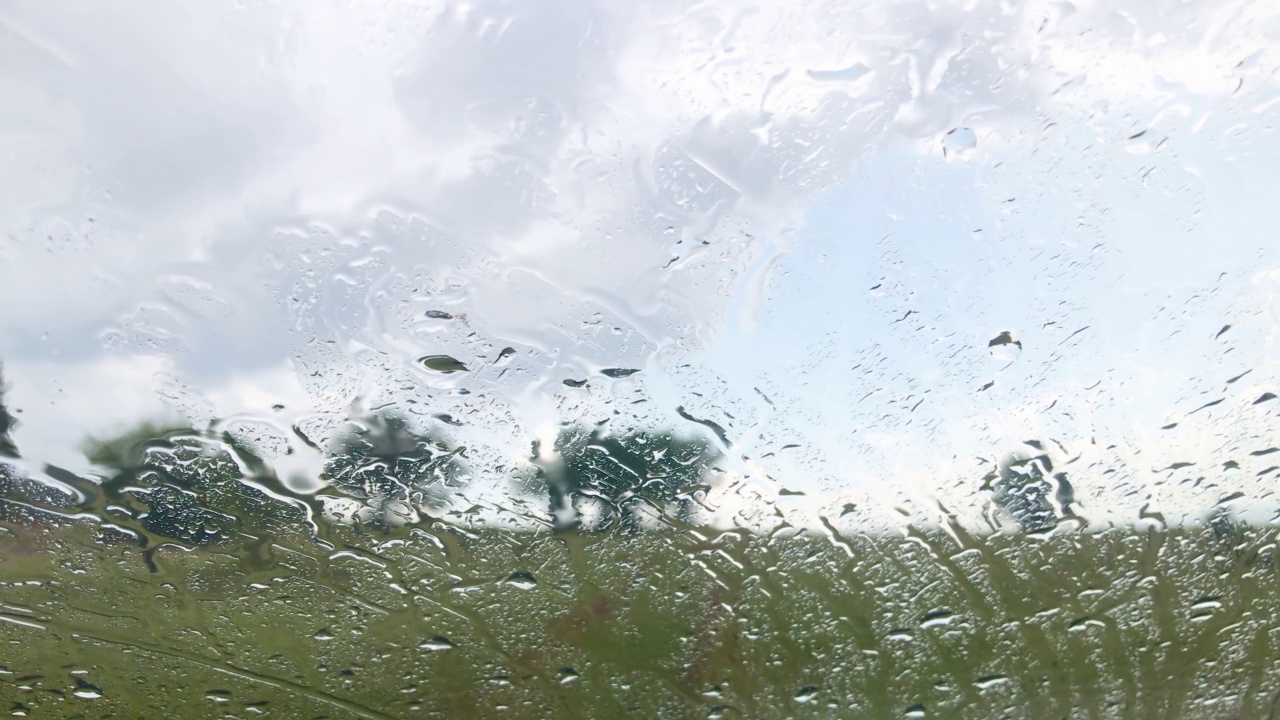 车窗上的雨滴模糊了汽车挡风玻璃上的树木和草地。多云的视频下载