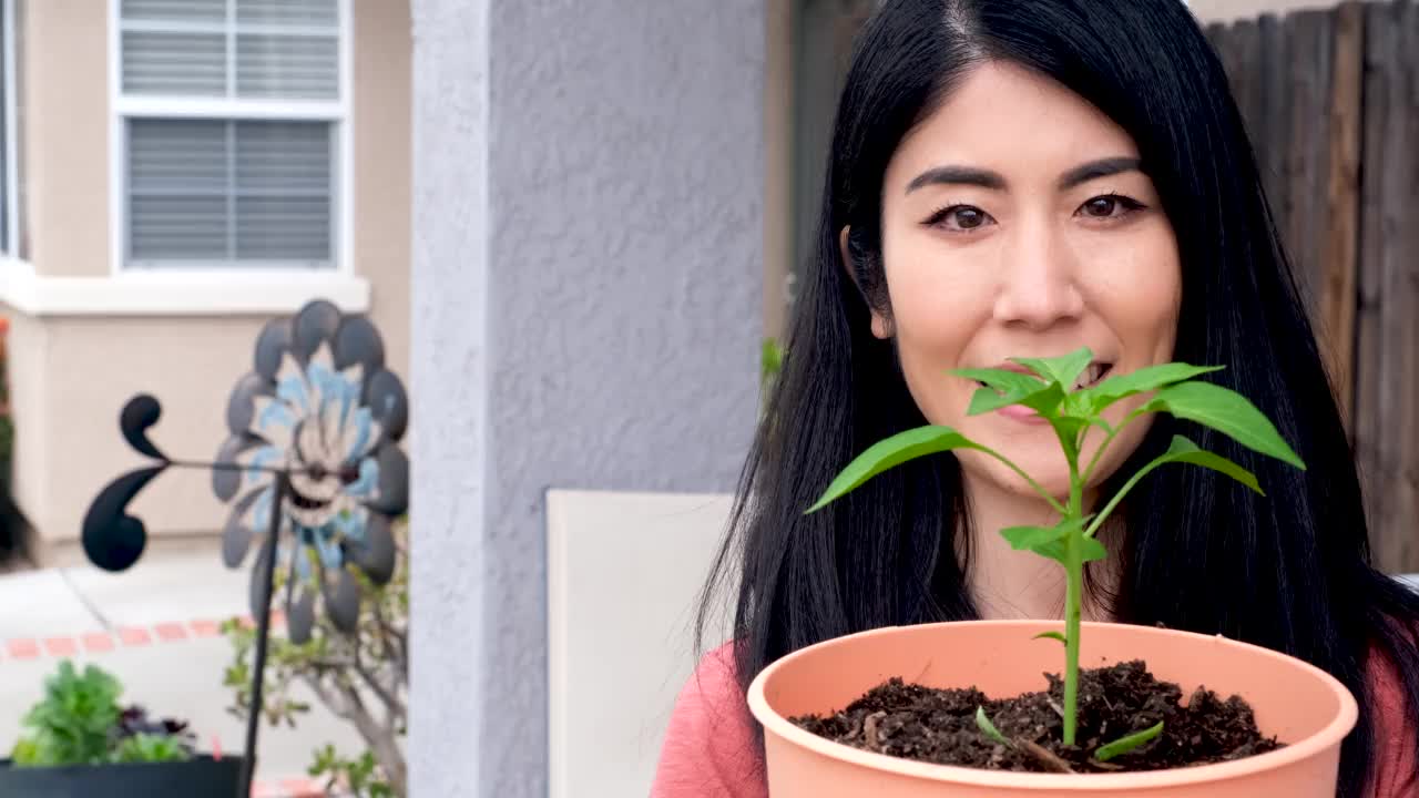 亚洲女人微笑着摆姿势看着相机，手里拿着一个花盆和一株植物视频素材