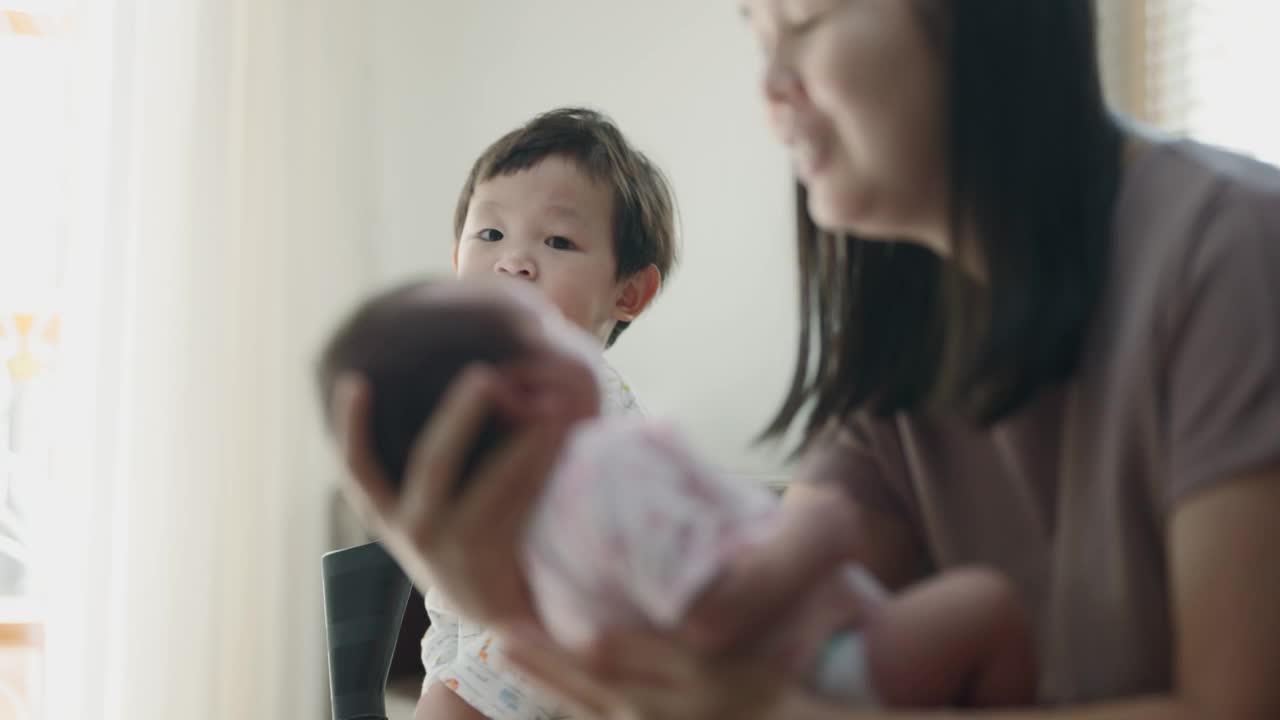 可爱的弟弟亲吻着妈妈膝上的弟弟。视频素材