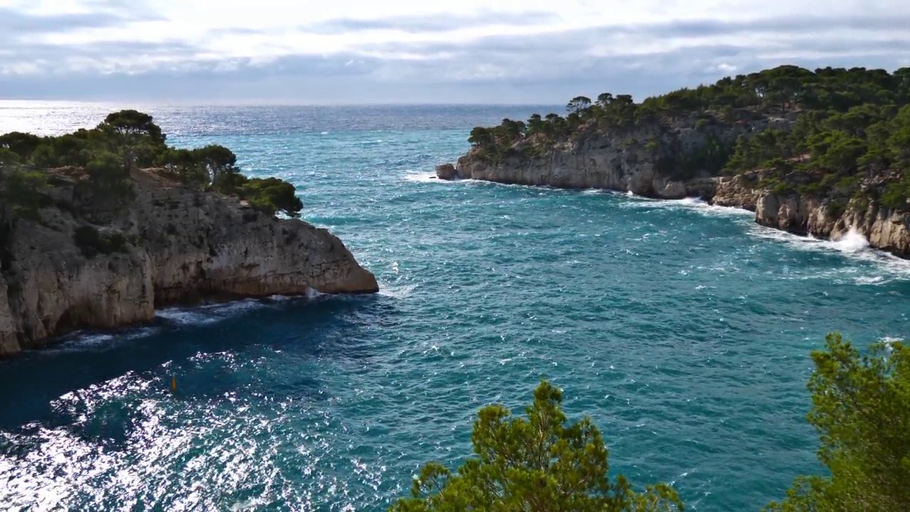 秋天，在法国南部里维埃拉的卡西斯附近的Calanque de Port-Miou海湾，在绿色松树覆盖下的独特岩石上，可以看到波涛汹涌的地中海。视频素材