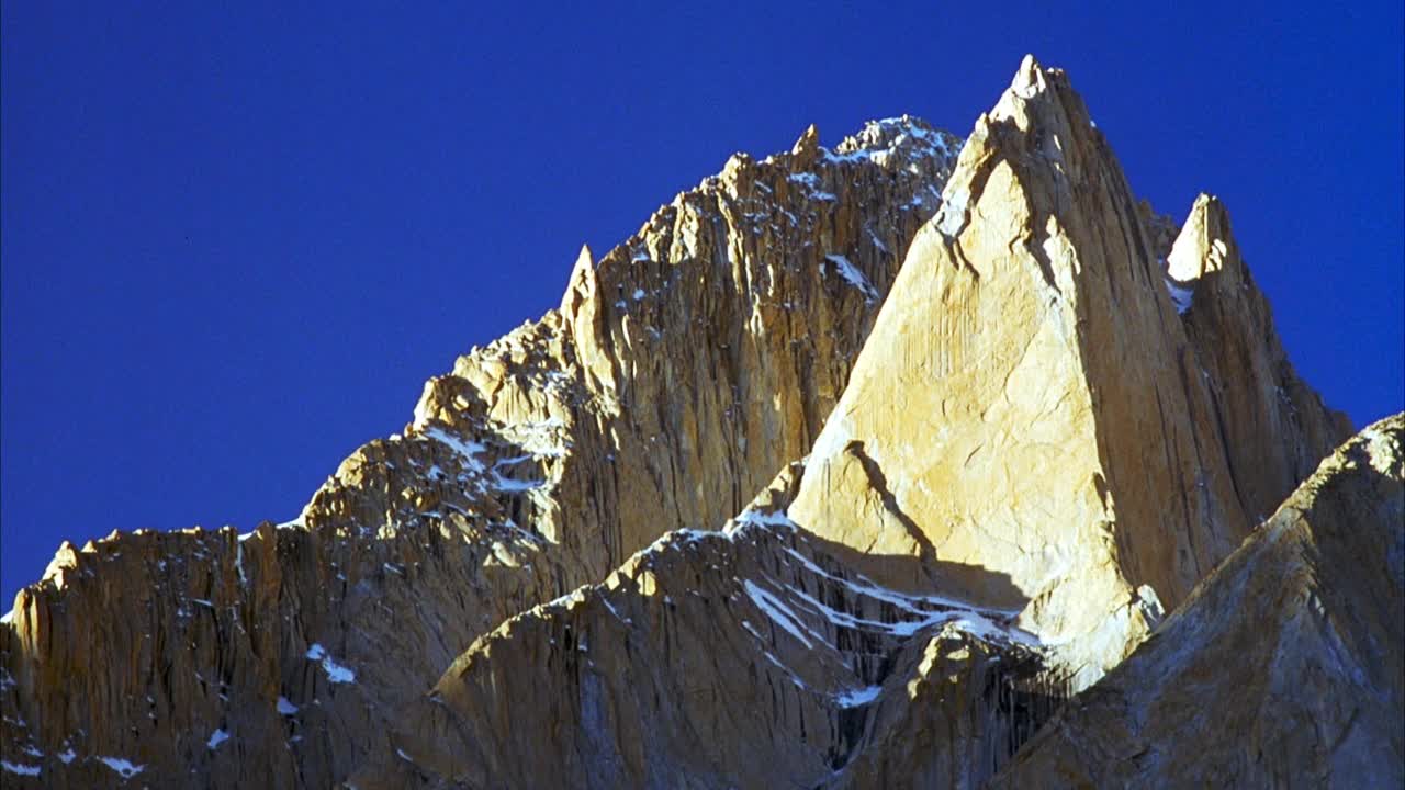 上角极其崎岖的山峰与剪切岩石悬崖。其中一个峰的形状像金字塔。在一些岩石表面看到阳光，而其他岩石表面或悬崖在阴影中。看到深邃清澈的蓝天。视频素材