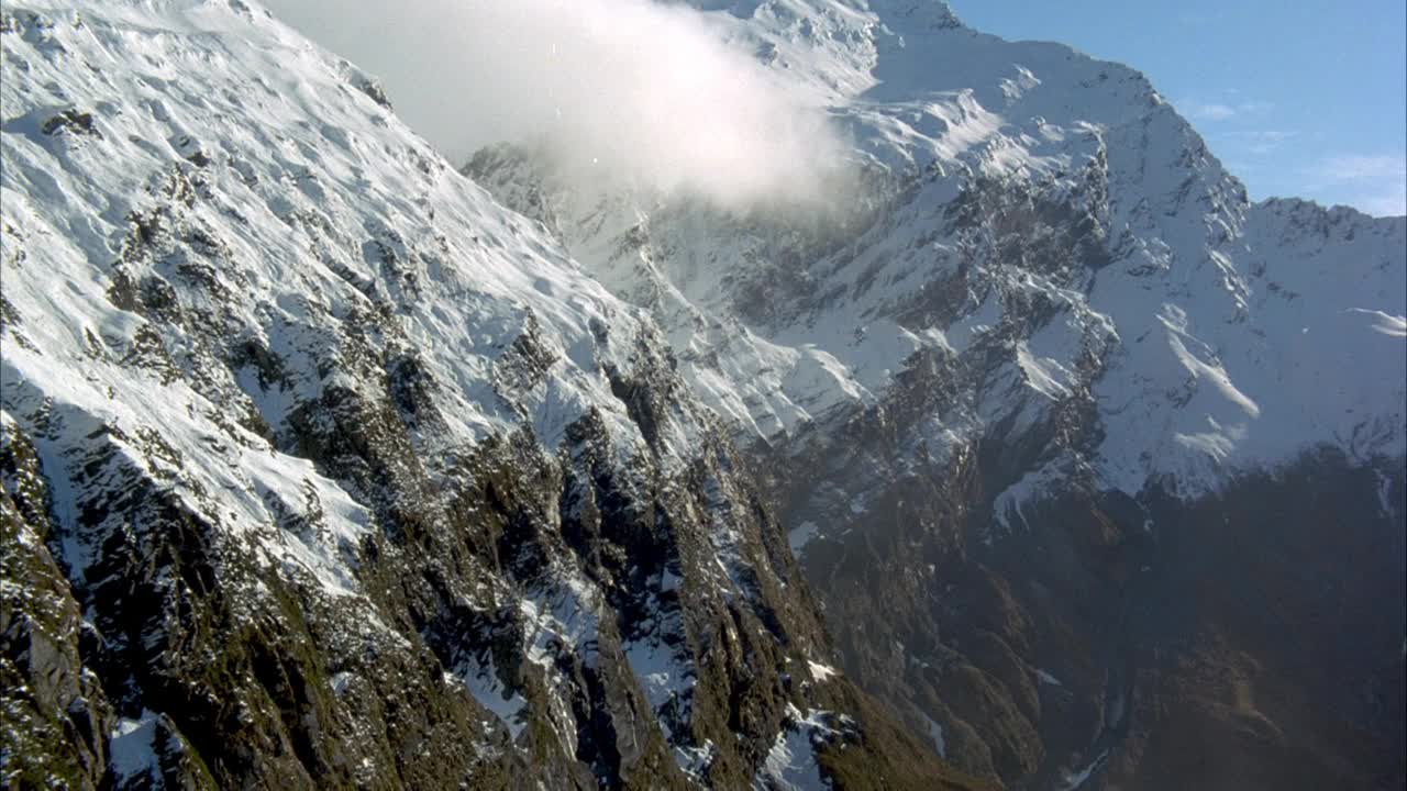 在雪山的岩石斜坡上空中飞行。在右边看到直升机的机头，镜头被太阳照射。视频素材