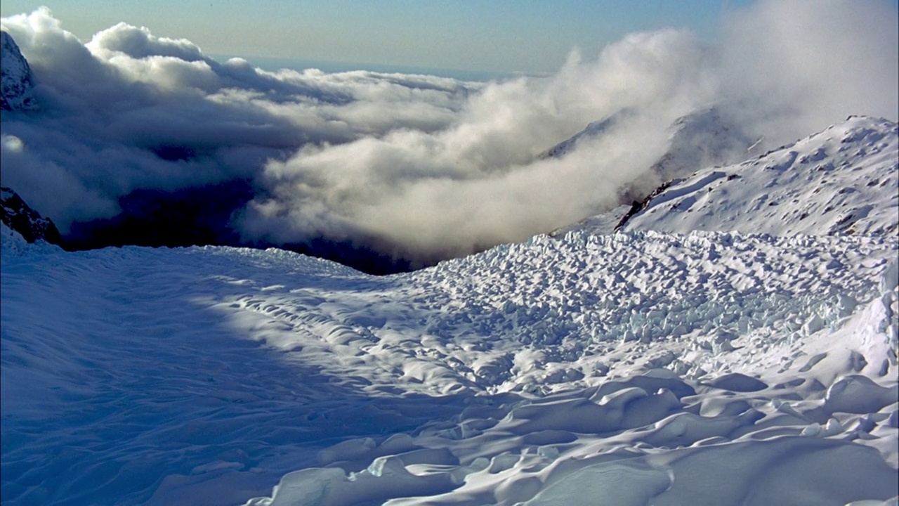 左潘下山积雪覆盖的山坡到纹理厚重的冰川积雪覆盖。在背景中可以看到低密度的云层挡住了大部分雪山的山峰。视频素材