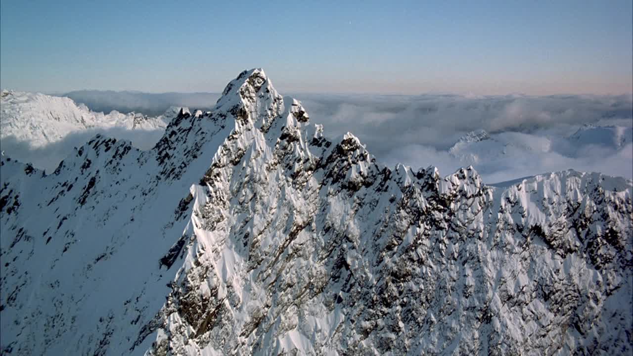 雪山山脊的天线。当波峰飞向山脊另一侧时，集中于小峰或小峰。当pov飞向山脊的原侧并往后拉时，集中在第二侧翼。在背景中看到雪山，较低的斜坡被低密度的积雨云遮蔽视频素材