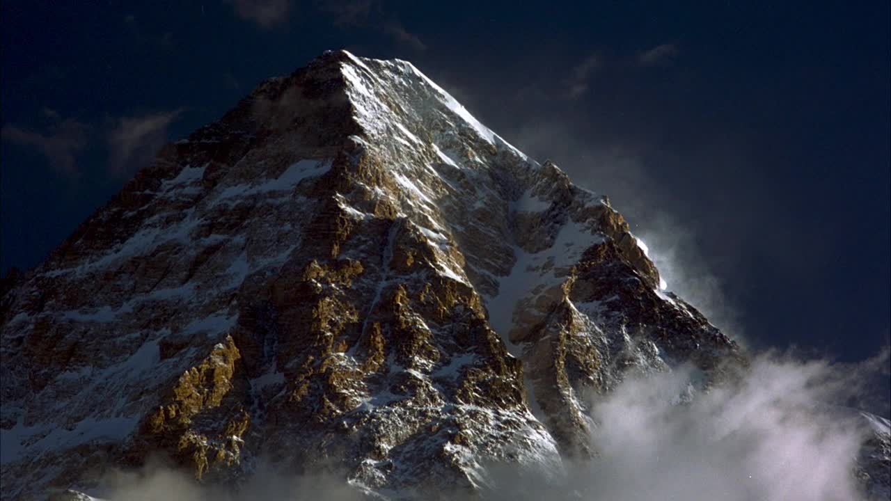 雪山峰顶中角。看稀疏的云框架的侧面和底部。在背景中看到清澈的蓝天。视频素材