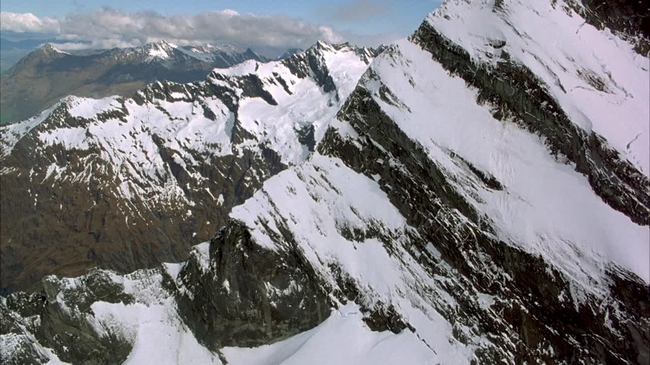 在白雪皑皑的山脊或山崖上空飞行。当苍蝇飞向另一边时，集中于山脊的边缘或峰。看到雪山低积云阻碍山峰和多云天空的背景。视频素材