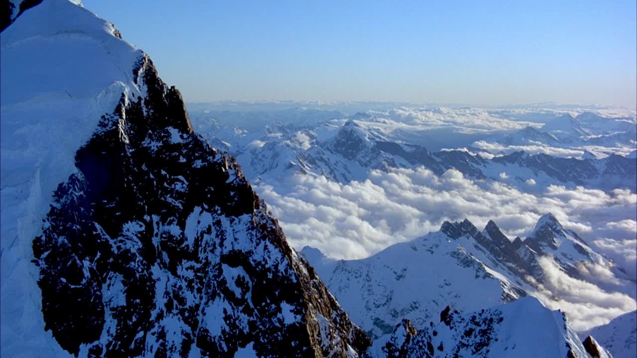 在白雪皑皑的山脊或山崖上空飞行。当苍蝇飞向另一边时，集中于山脊的边缘或峰。看到雪山和清澈的蓝天背景。视频素材