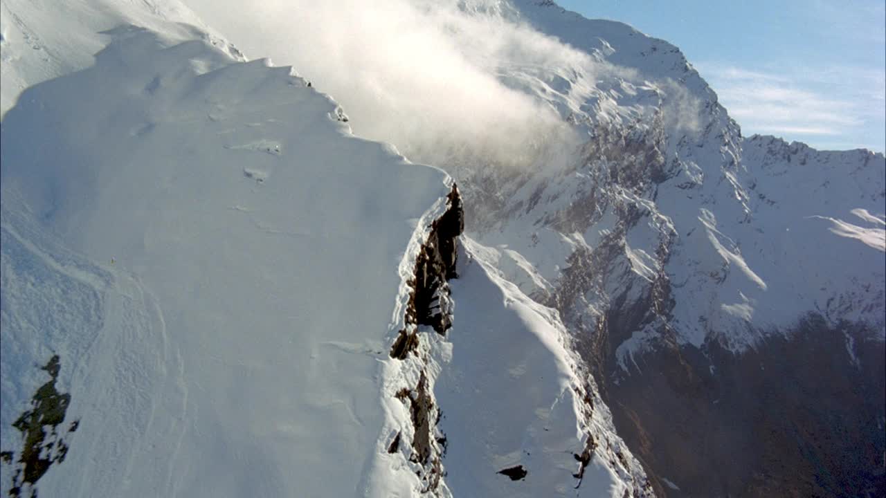 在积雪覆盖的山坡上，云雾从上面滚下来。在背景中可以看到蓝天和雪山。视频素材