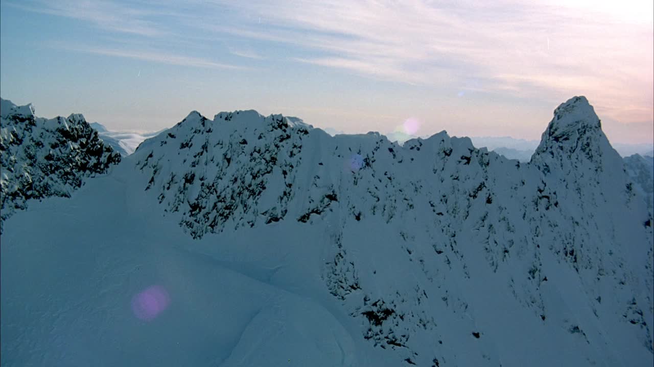 空中朝向雪山山脊或山脊。镜头光晕,晕光。当坡面逆时针旋转时，聚焦于山脉的边缘。在背景中看到雪山。视频素材