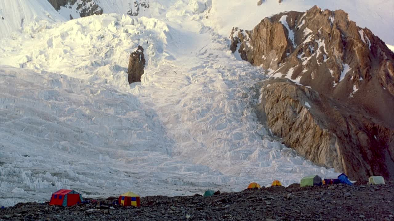 在积雪覆盖的山坡上，五颜六色的帐篷固定在岩石地面上。视频素材