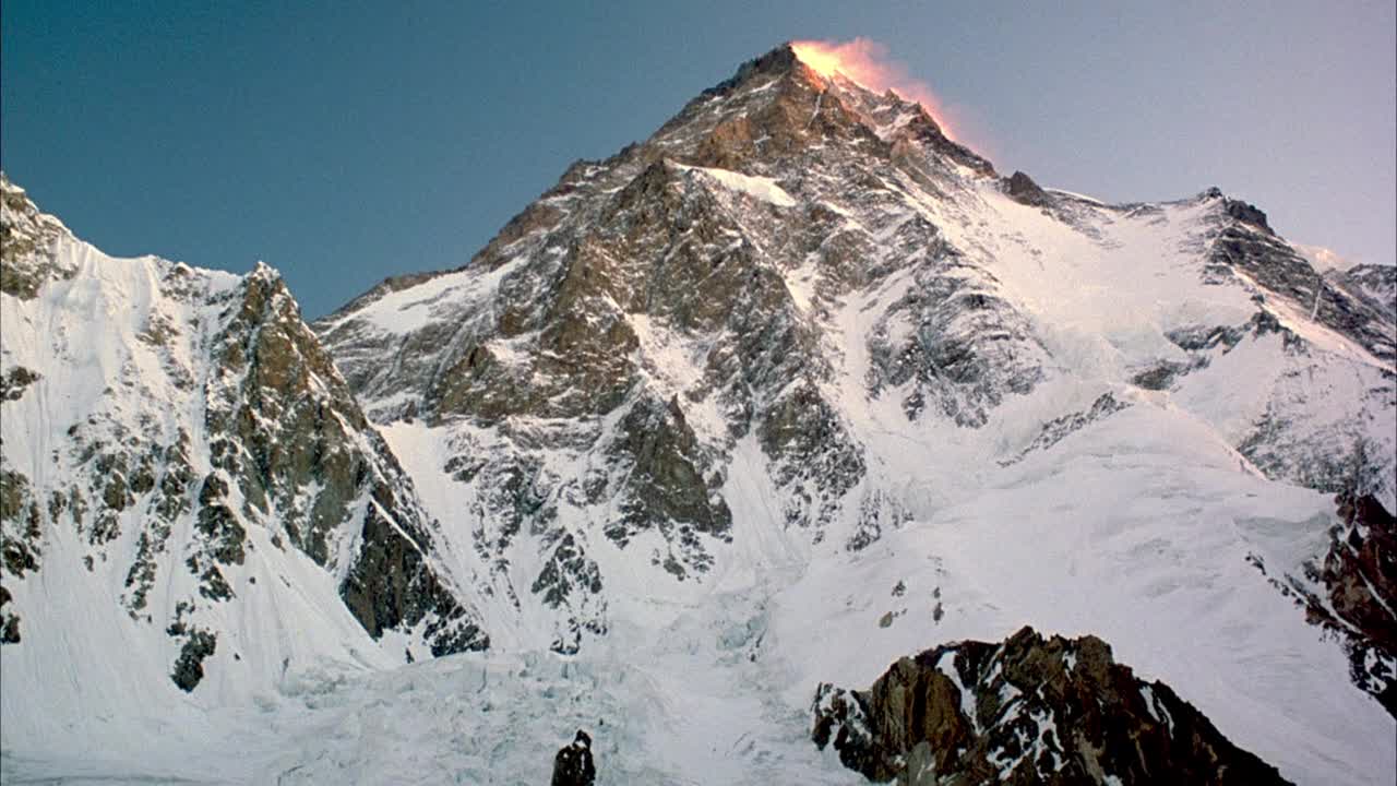 雪山峰顶中角。看到粉红色或玫瑰色的雾或云从太阳在屏幕右侧滚动的右边边缘的峰。在背景中看到清澈的蓝天。视频素材