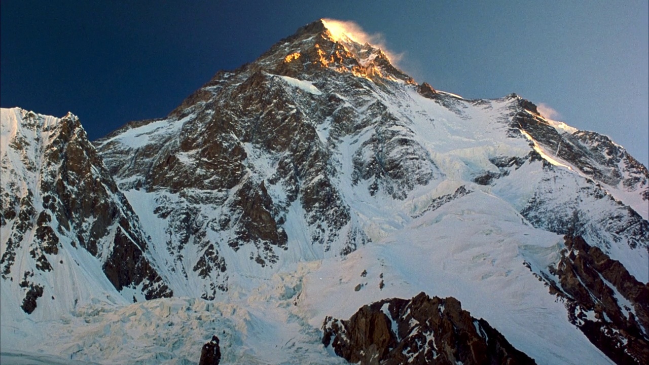 雪山峰顶中角。看到金色的雾或云从太阳从右边滚动的峰的右边边缘。在背景中看到清澈的蓝天。视频素材