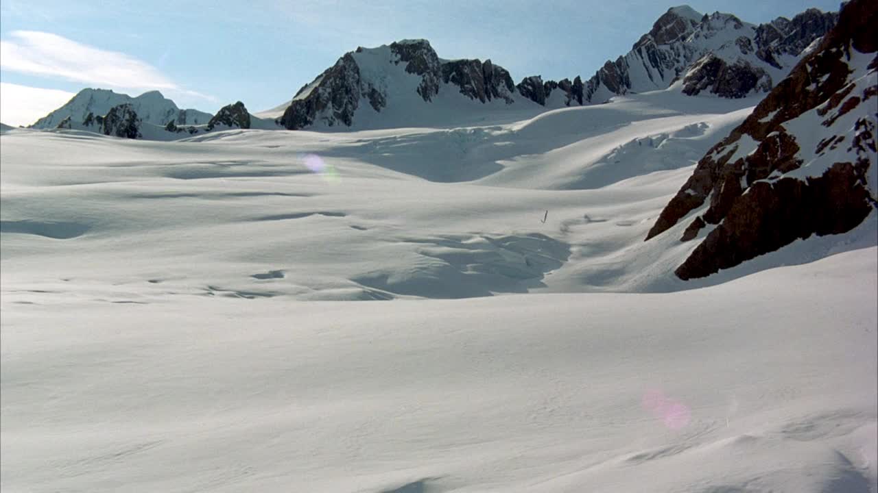 在积雪覆盖的地面和冰川形成的空中拍摄。在背景中看到雪山。看有卷云的蓝天。看镜头从太阳耀斑。视频素材