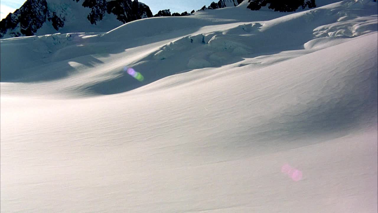 在积雪覆盖的地面和冰川形成的空中拍摄。在背景中看到雪山。看有卷云的蓝天。看镜头从太阳耀斑。视频素材