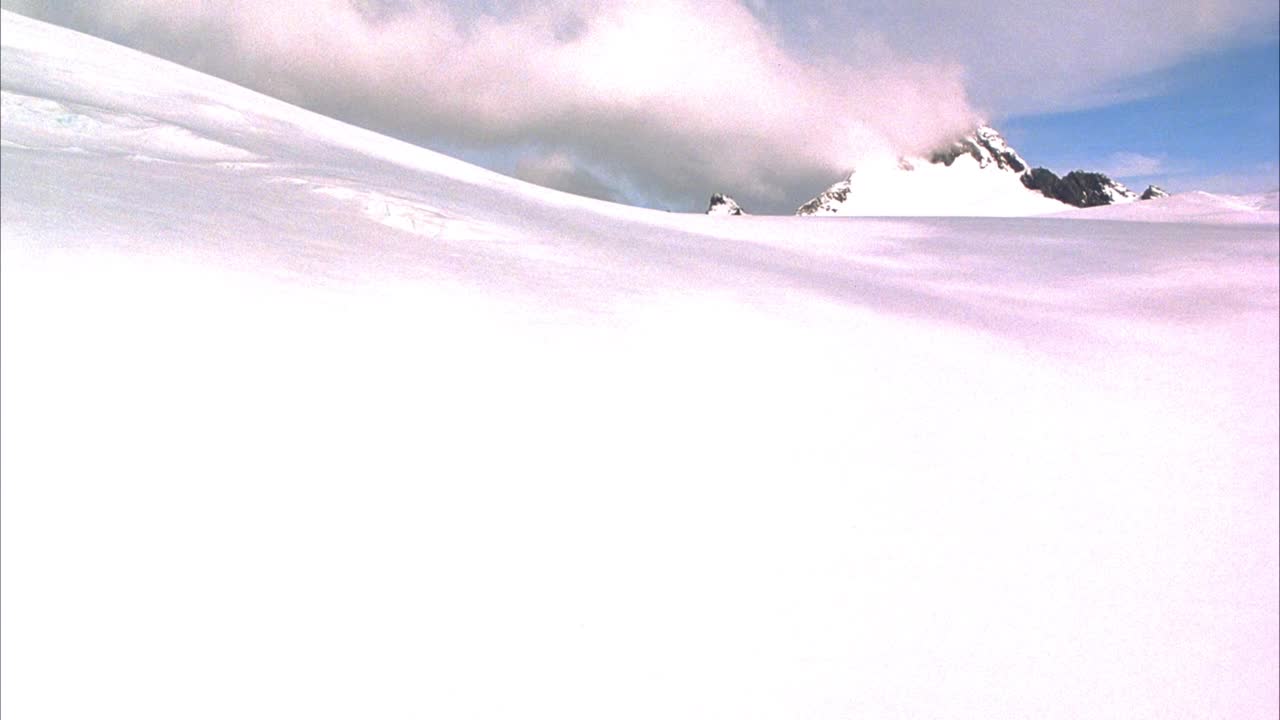 在冰雪覆盖的地面和冰川上空飞行。看pov飞过冰川的构造。背景中可以看到雪山和积云。视频素材