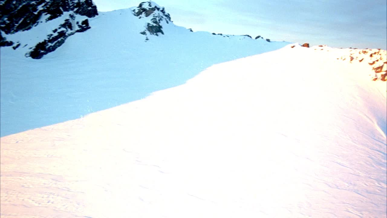 空中的积雪覆盖的山脉作为背景。相机从右到左平移，在背景中看到更多积雪覆盖的山脉。看到蓝色的天空。视频素材