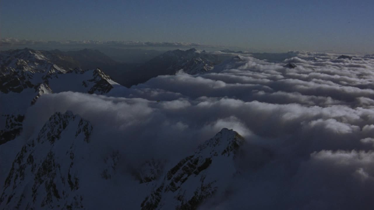 白色积云的空中覆盖物。看雪山。看到山顶与白色积云毯子在底部和周围的山脉。看波峰从云天的一边飘到另一边。用光晕和透镜光圈看太阳视频素材