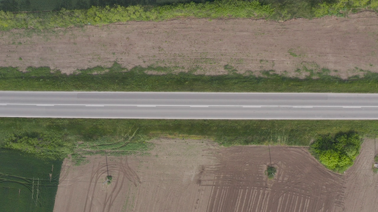 俯瞰黑色客车在直公路通过农村景观，无人机pov空中拍摄视频素材