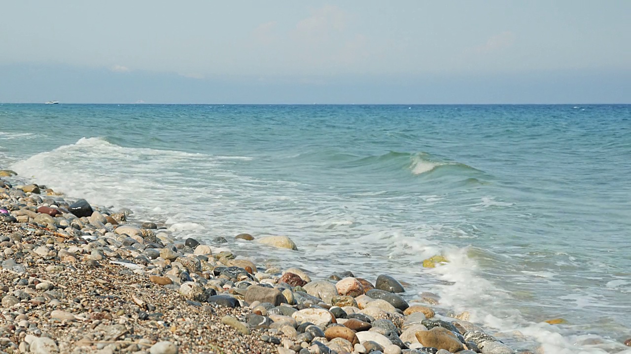 海浪拍打着卵石滩。夏天的海景。清澈的蓝绿色海水拍打在石头和鹅卵石上。夏日沙滩旅行概念视频素材