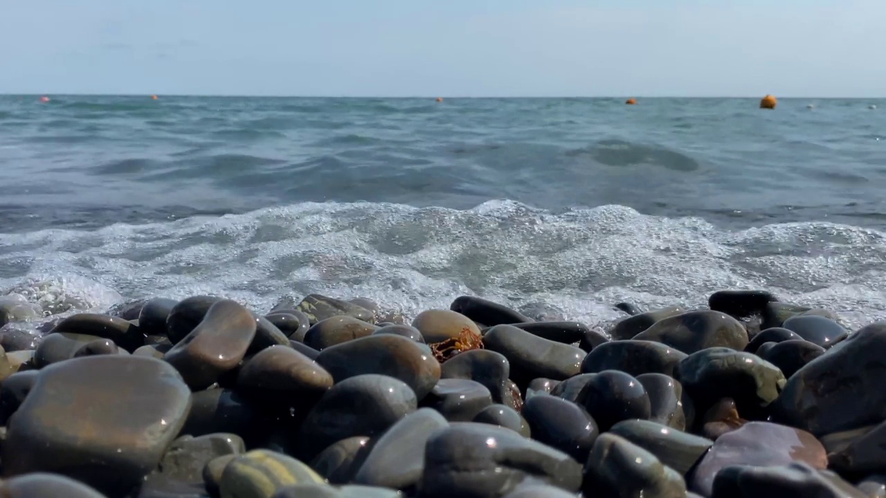 孩子们穿着泳鞋、海浪和卵石滩在海水上奔跑。慢动作视频视频素材