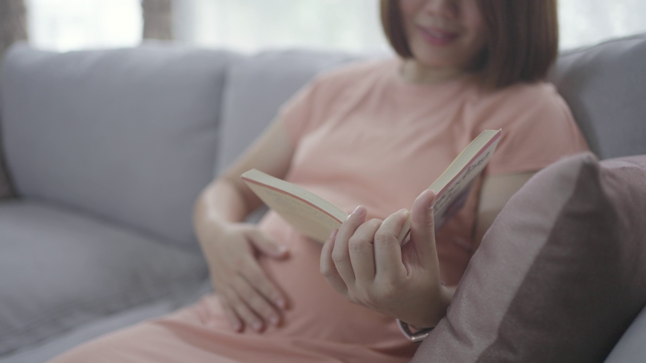 怀孕的亚洲妇女阅读一本书休息时间与她的婴儿视频素材