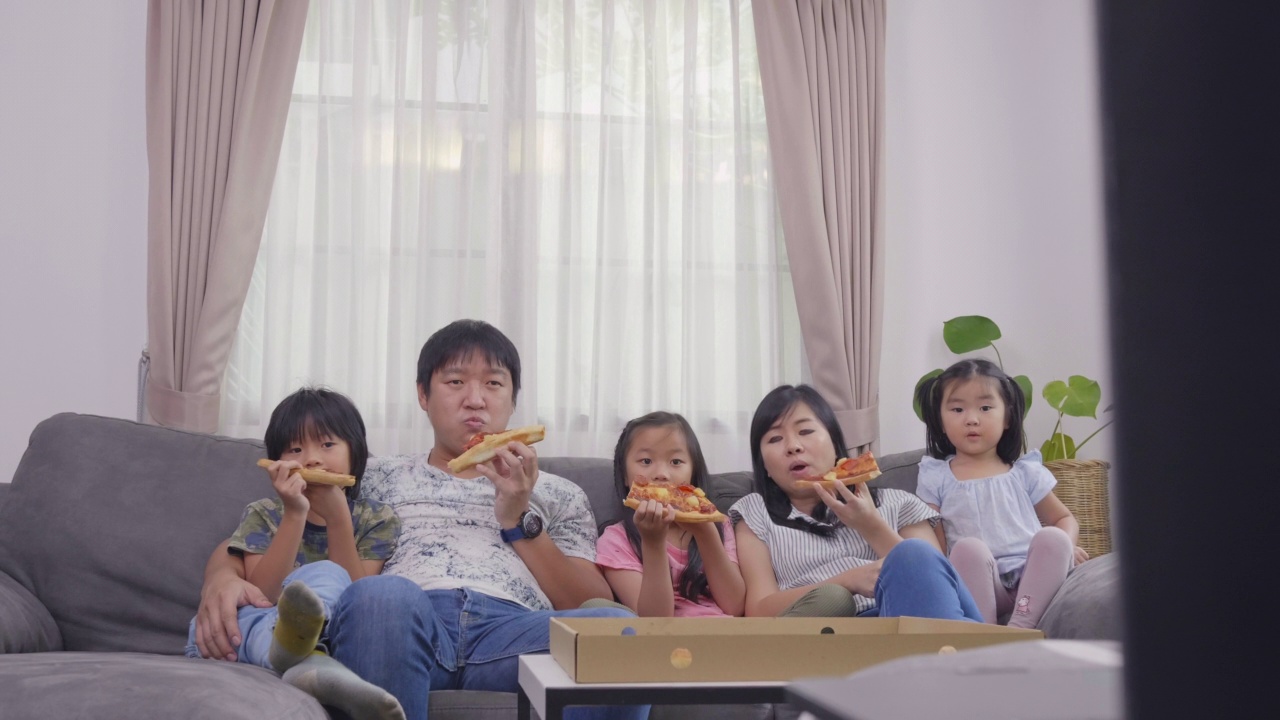 幸福的亚洲家庭喜欢在假日在家的沙发上吃披萨和看电视视频素材画面2