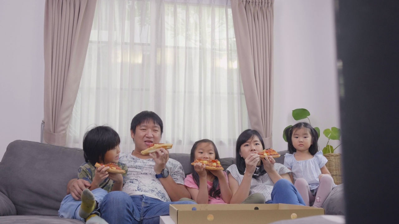 幸福的亚洲家庭喜欢在假日在家的沙发上吃披萨和看电视视频素材画面4