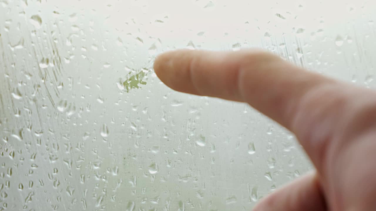 人在雾蒙蒙的窗户上画心，窗外有雨滴视频素材