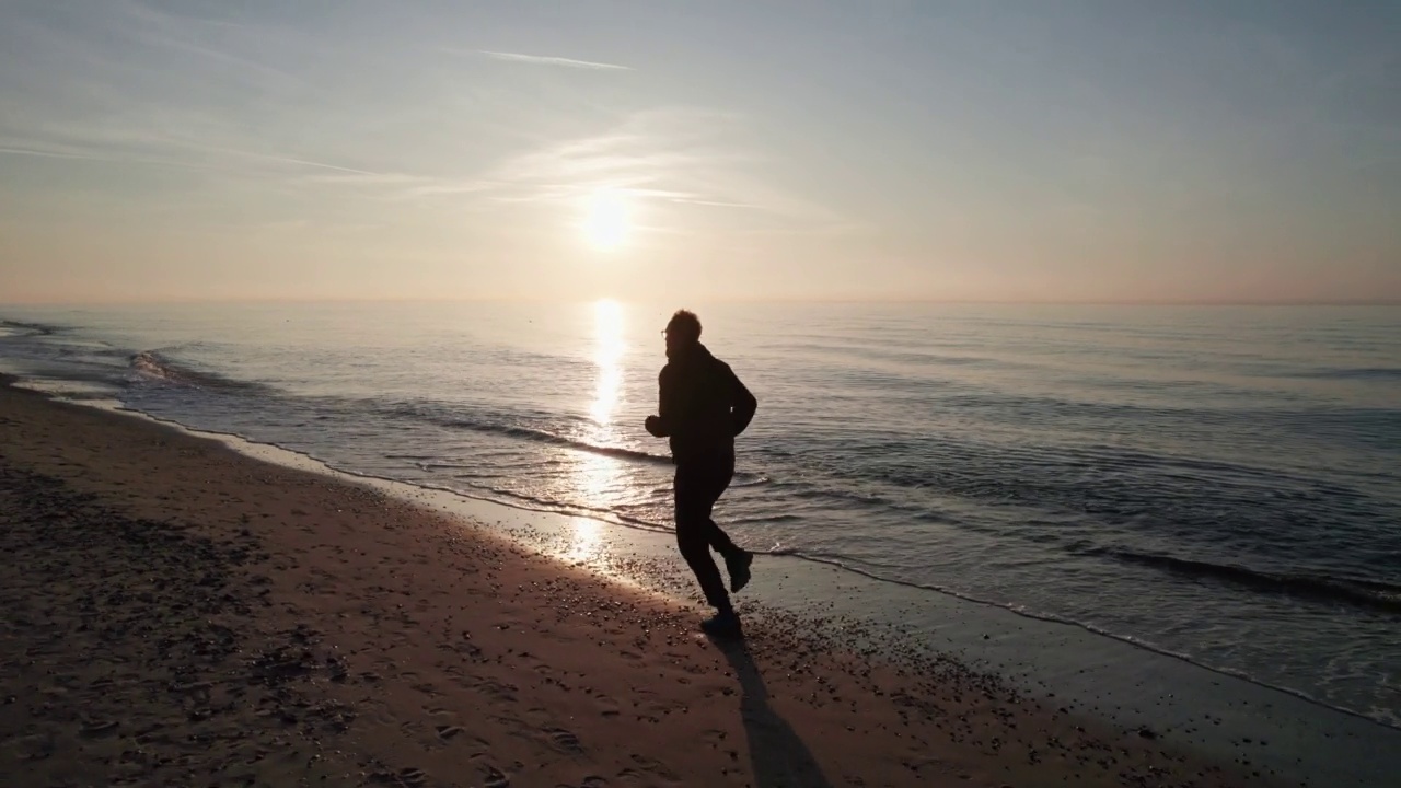 穿着运动服的人跑过海滩，夕阳西下。视频素材