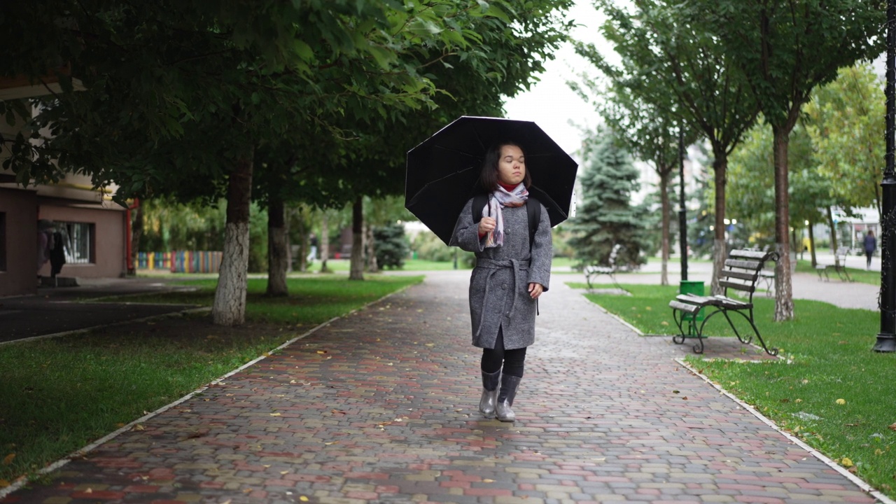 忧伤的小女人在夏日的雨天撑着伞在户外散步。正面视图宽镜头肖像深思熟虑的高加索小人儿走在城市街道户外慢动作离开。视频素材