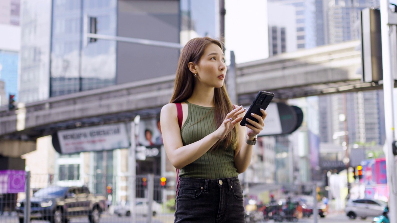 一名亚洲女子在马来西亚吉隆坡旅行时，站在武吉斌棠路口使用智能手机。视频素材