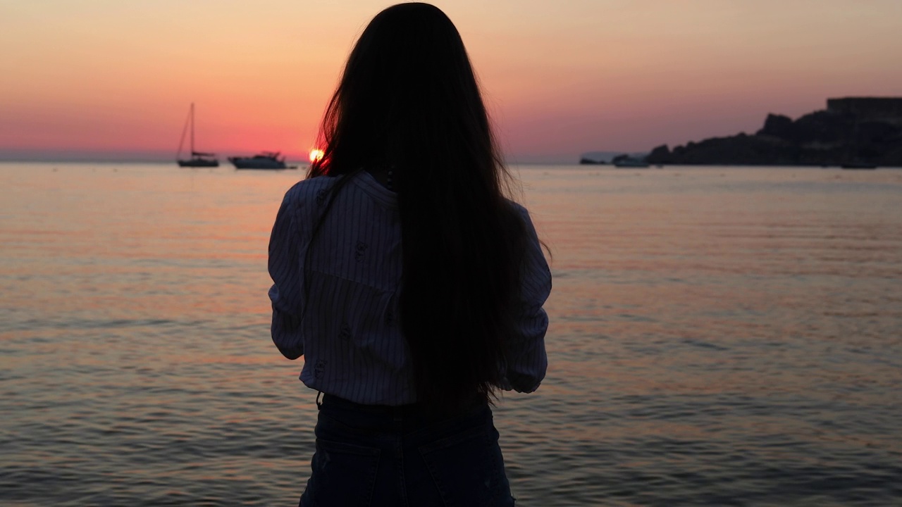 年轻女子在海滩上拍摄美丽的日落视频素材