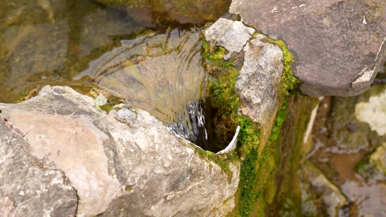 将纯净的泉水从天然的石质苔藓容器中引流到金属落水管中视频素材