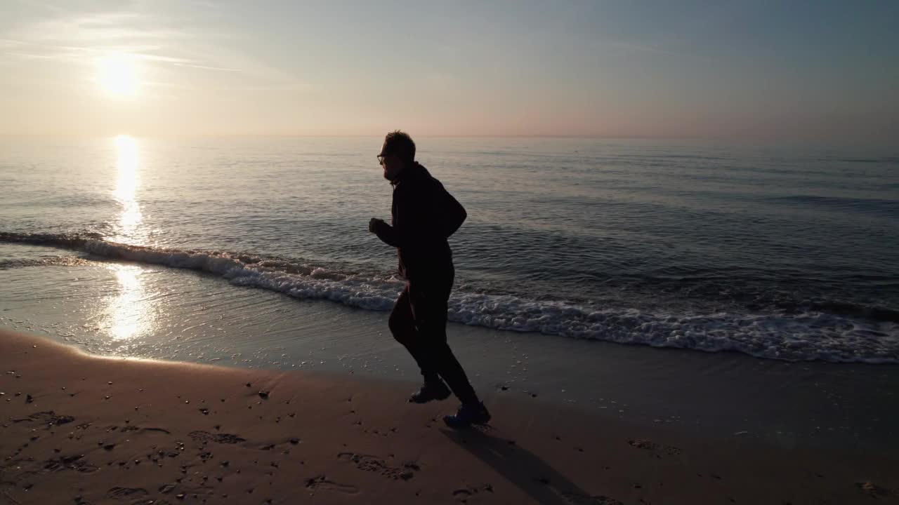 穿着运动服的人跑过海滩，夕阳西下。视频素材