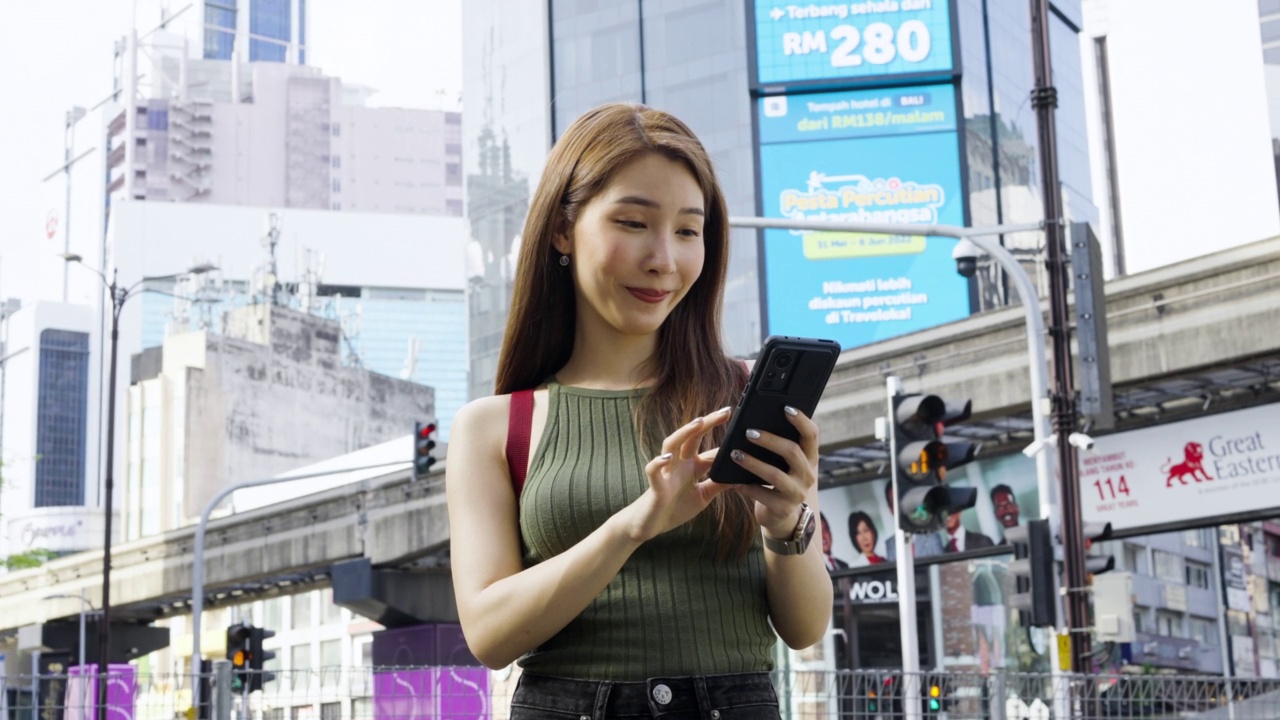 一名亚洲女子在马来西亚吉隆坡旅行时，站在武吉斌棠路口使用智能手机。视频素材