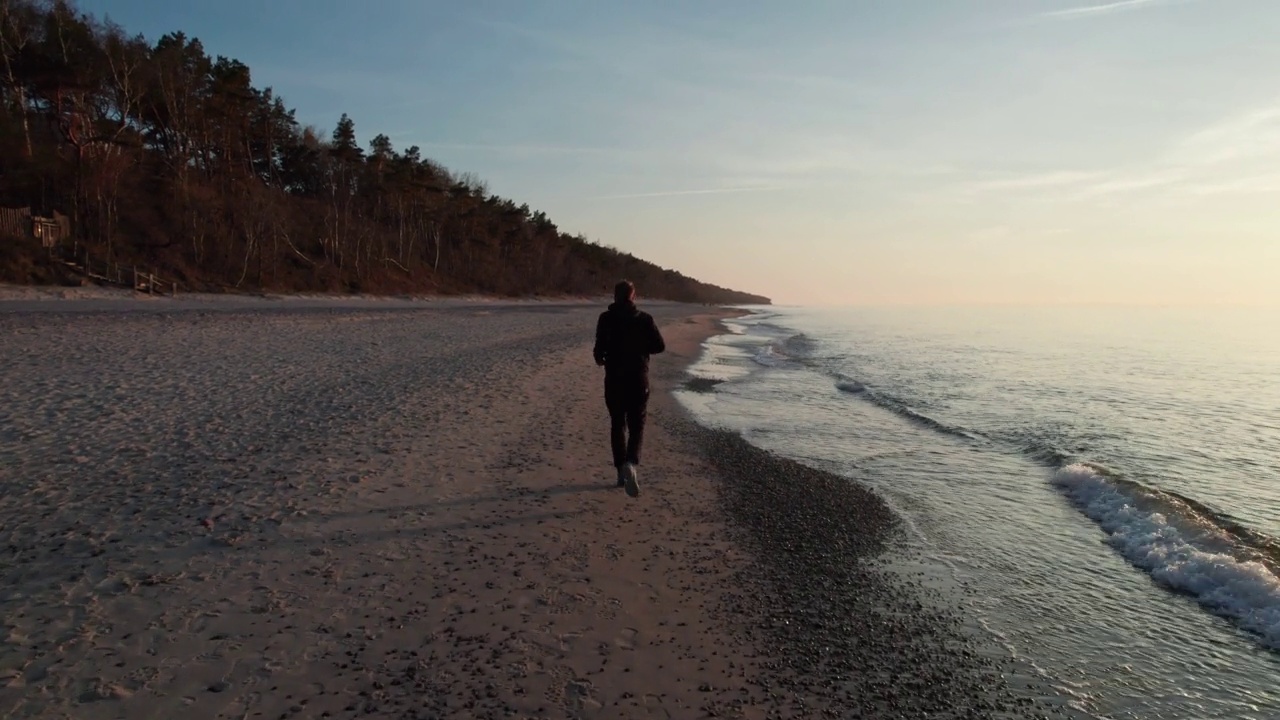 穿着运动服的人跑过海滩，夕阳西下。视频素材