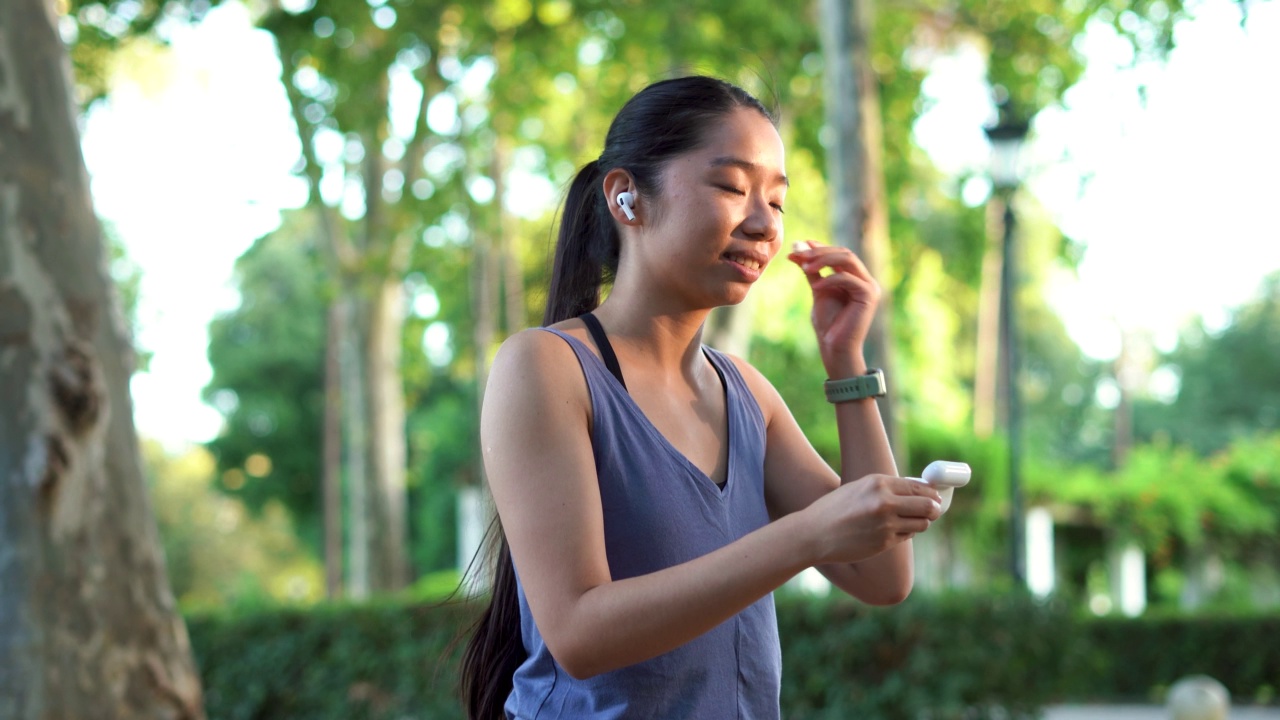 亚洲运动女孩在公园跑步前打开无线耳塞的案例视频素材