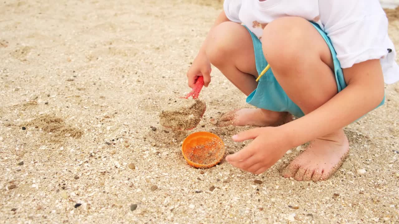 可爱的白人小男孩在海边玩沙滩玩具和沙子。视频素材