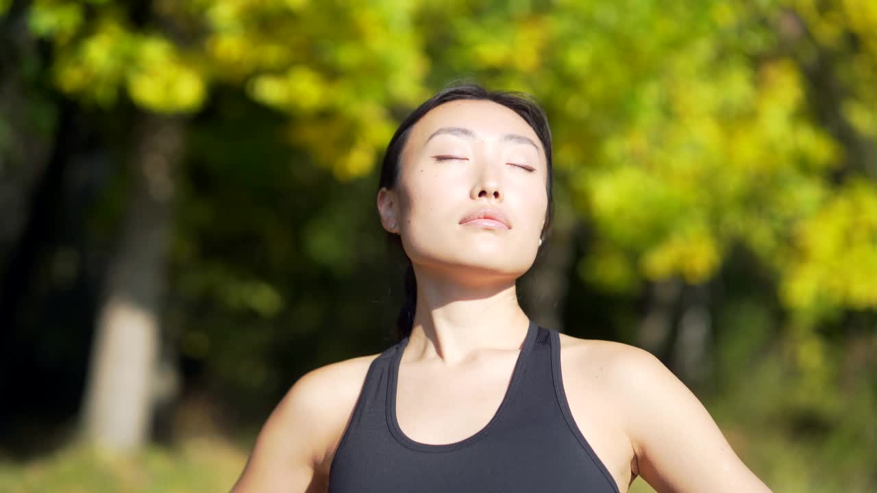 特写肖像年轻快乐fit亚洲妇女站在森林树木之间的自然放松，呼吸新鲜空气闭上眼睛。女性享受平静平静的生活视频素材