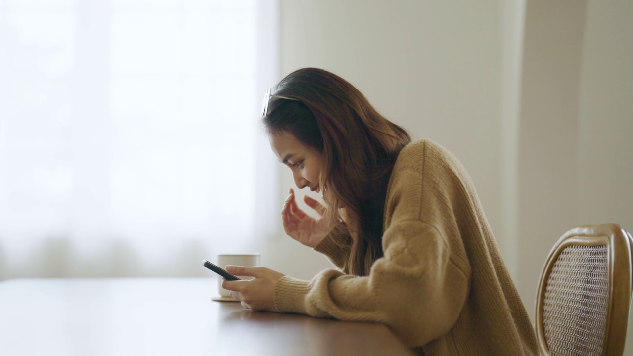 兴奋的亚洲女性使用智能手机。年轻的亚洲女人在家里快乐和微笑视频素材