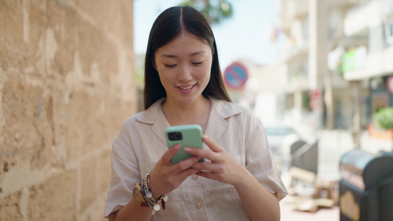 中国女子自信地微笑着在街上使用智能手机视频素材