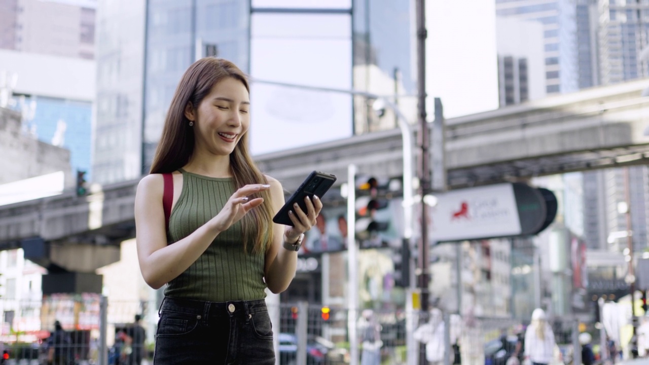 一名亚洲女子在马来西亚吉隆坡旅行时，站在武吉斌棠路口使用智能手机。视频下载